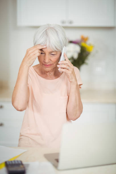 istock Tensed senior woman talking on mobile phone in kitchen 645438980