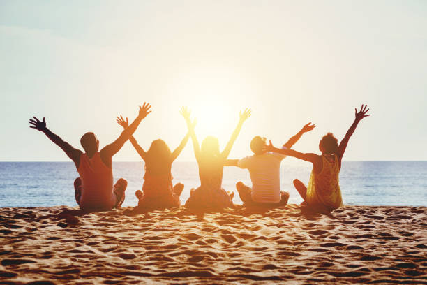 Group happy people beach sea sunset concept Group of five happy people sits on background of empty sunset beach. Travel or sea vacations concept summer fun stock pictures, royalty-free photos & images