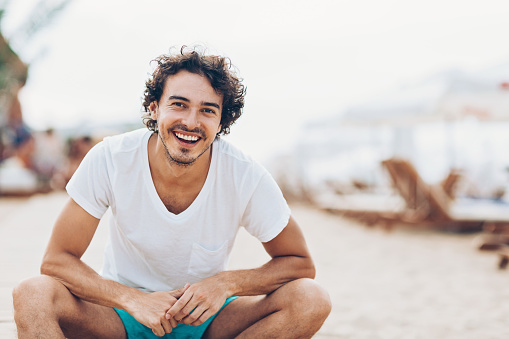 Cheerful young man sitting on the beach in the summer, with copy space
