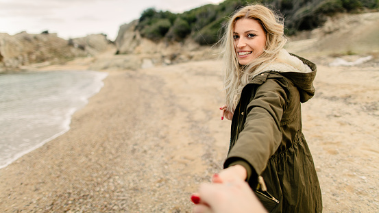 Young smiling woman at the beach, holding hands with her boyfriend