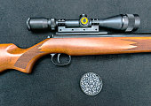 Air gun with wooden butt, scope and pellets on a black background