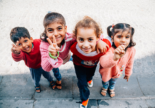 Four unidentified happy Syrian children having fun and some are making a peace sign while looking at the camera on street of Balat, Istanbul, Turkey