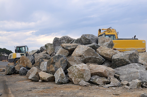 A heavy load of large rocks for rebuilding the breakwater along the Chesapeake Bay with construction equipment in the background