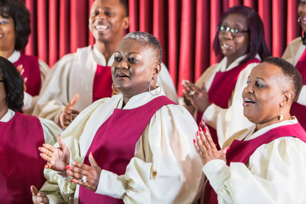 Mature black women and men singing in church choir A group of mature African American women and men wearing robes, singing and clapping in a church choir. black female gospel singers stock pictures, royalty-free photos & images