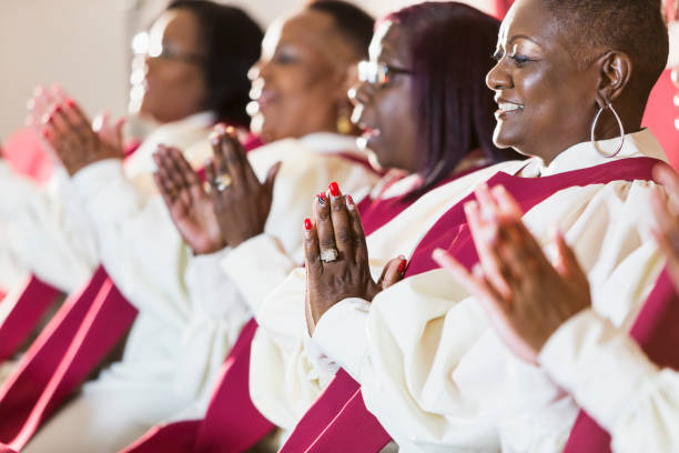 Group of mature black women in church robes A group of mature black women in church robes, sitting in a row, clapping. They are members of the church choir listening to a sermon. gospel stock pictures, royalty-free photos & images