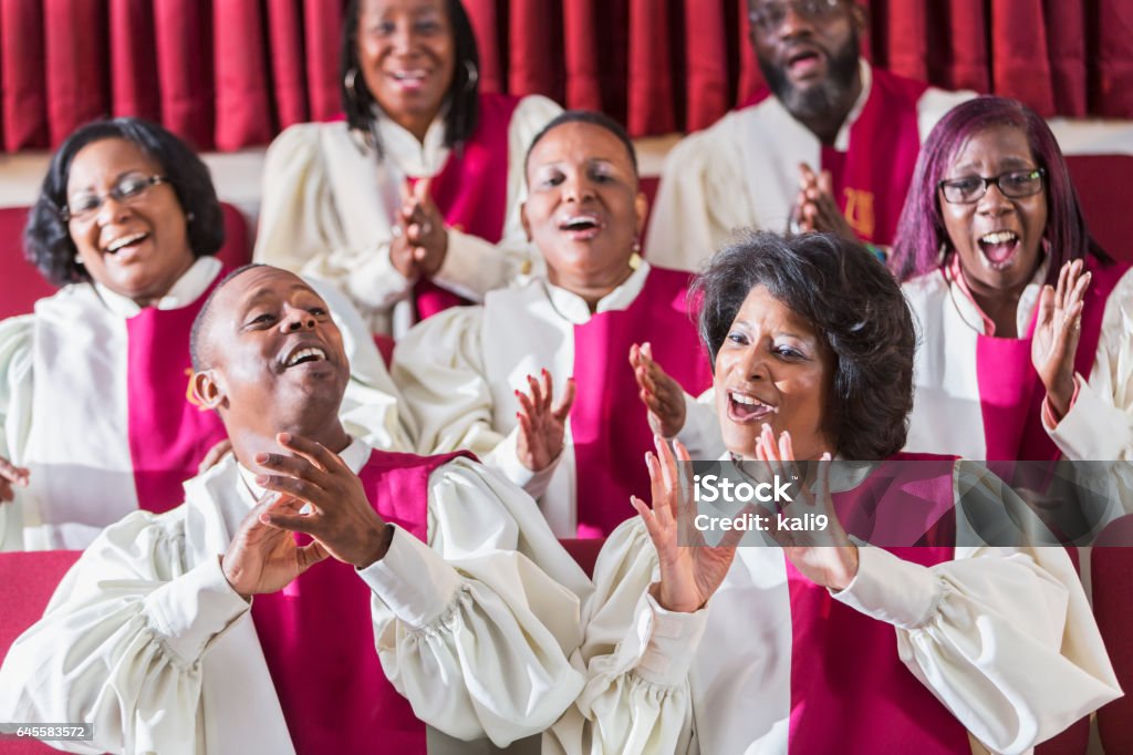 Mature black women and men singing in church choir A group of mature African American women and men wearing robes, singing and clapping in a church choir. Choir Stock Photo