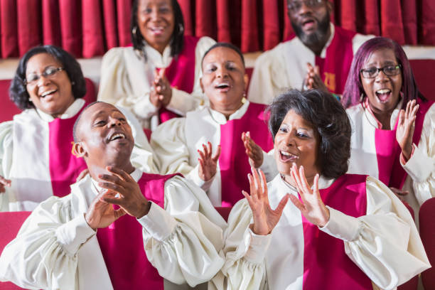 Mature black women and men singing in church choir A group of mature African American women and men wearing robes, singing and clapping in a church choir. choir photos stock pictures, royalty-free photos & images
