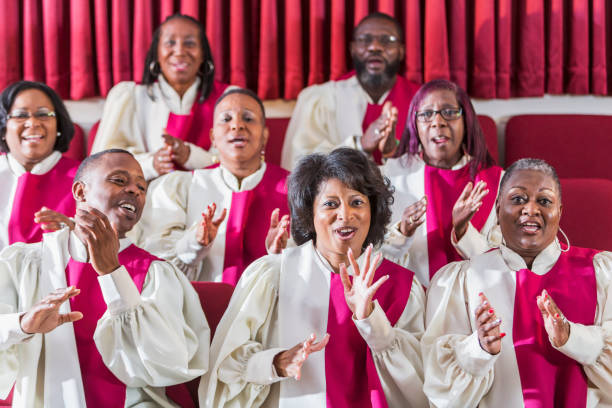 Mature black women and men singing in church choir A group of mature African American women and men wearing robes, singing and clapping in a church choir. gospel stock pictures, royalty-free photos & images