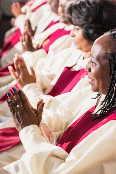 Group of mature women in church robes sitting A group of mature black women in church robes, sitting in a row, clapping. They are members of the church choir listening to a sermon. The focus is on the woman in the foreground. black female gospel singers stock pictures, royalty-free photos & images