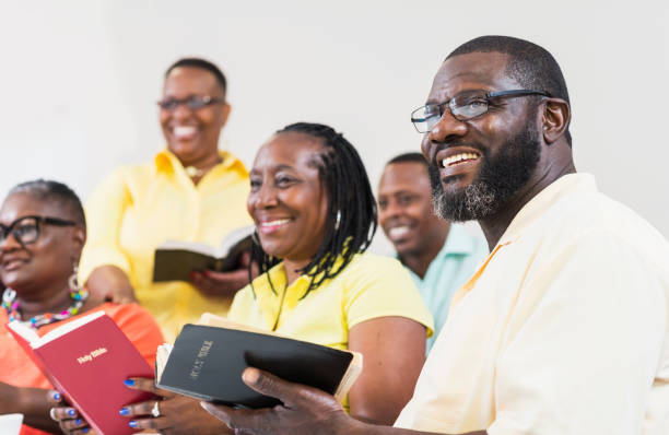Group of mature black men and women holding bibles A group of mature African-American men and women holding bibles. They are in a church meeting or bible study group, watching a presentation. The focus is on the man in the foreground wearing eyeglasses. bible study group of people small group of people stock pictures, royalty-free photos & images