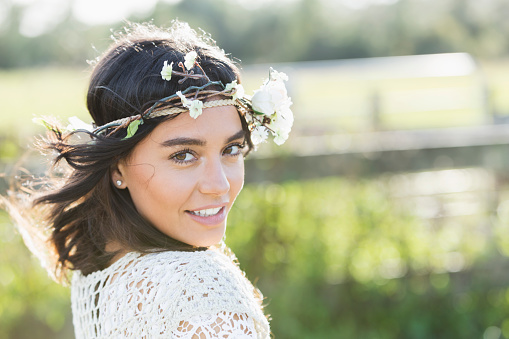A beautiful, young boho-chic Hispanic woman standing outdoors, smiling and looking at the camera.