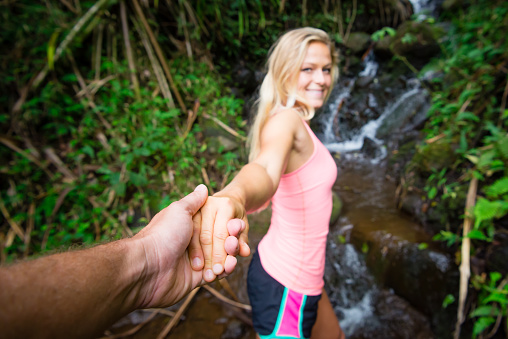 A young happy women leading her boyfriend into nature.  Focus is on the hands.