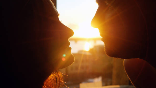 Romantic young couple in love looking each other on a sunset with sun shining bright behind them on a horizon. Romantic young couple silhouette is kissing on a sunset with sun shining bright behind them on a horizon. kissing on the mouth stock pictures, royalty-free photos & images