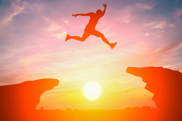Silhouette of man jump over the cliff obstacle in sunset stock photo