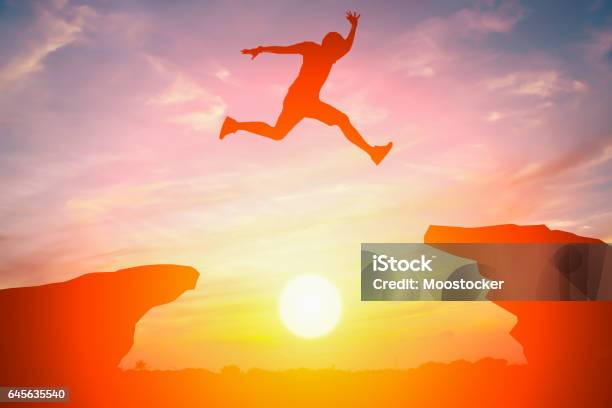 Silhouette Of Man Jump Over The Cliff Obstacle In Sunset Stock Photo - Download Image Now