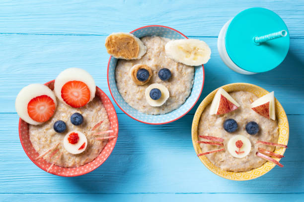 bols drôle avec gruau d’avoine aux visages, chien, chat et souris faite de fruits et de baies, de nourriture pour l’idée des enfants, vue de dessus - oatmeal breakfast healthy eating food photos et images de collection