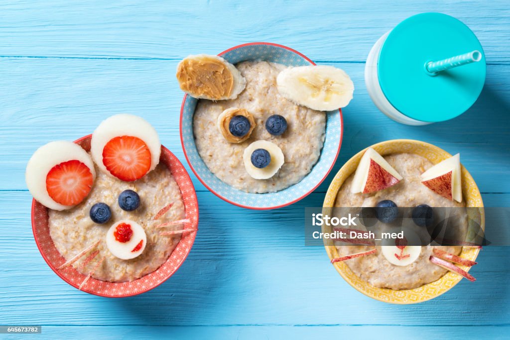 Funny bowls with oat porridge with cat, dog and mouse faces made of fruits and berries, food for kids idea, top view Funny bowls with oat porridge with cat, dog and mouse faces made of fruits and berries, food for kids idea, top view, blue wooden background Child Stock Photo