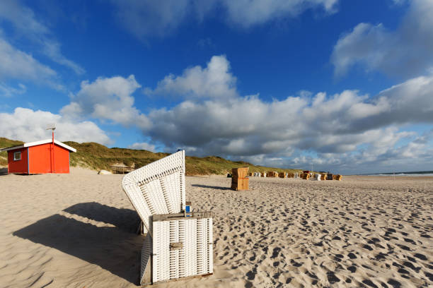 Summer beach landscape with wicker chairs, high grass dunes, and the North Sea water, on Sylt island, Germany. Sunny summer vacation context.