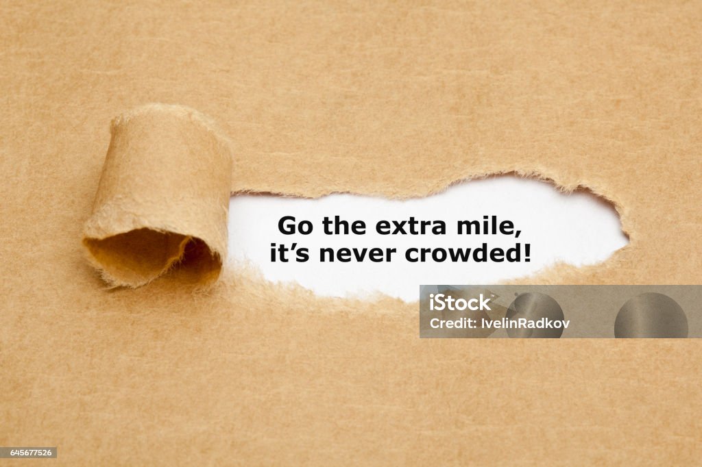 Go The Extra Mile Its Never Crowded Motivational quote Go The Extra Mile It's Never Crowded appearing behind ripped brown paper. Dedication Stock Photo