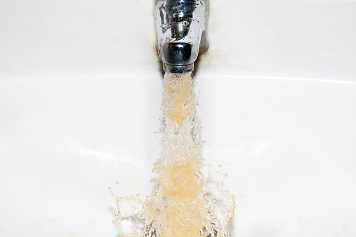 Polluted brown running water falling into a white sink from tap