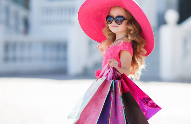 cute little girl in fashion hat with shopping bags next to a supermarket - fashion model small one person happiness imagens e fotografias de stock