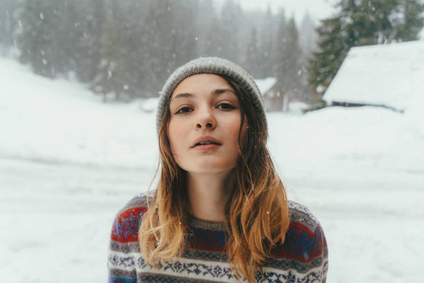 Young Caucasian woman in sweater standing outdoors on the background of pine tree forest in winter