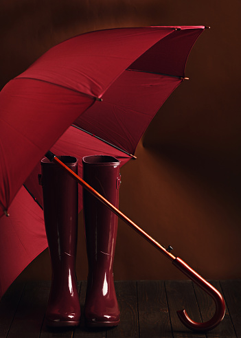 Photo in low key. Rubber boots and umbrella burgundy color on a brown background. Selective focus.