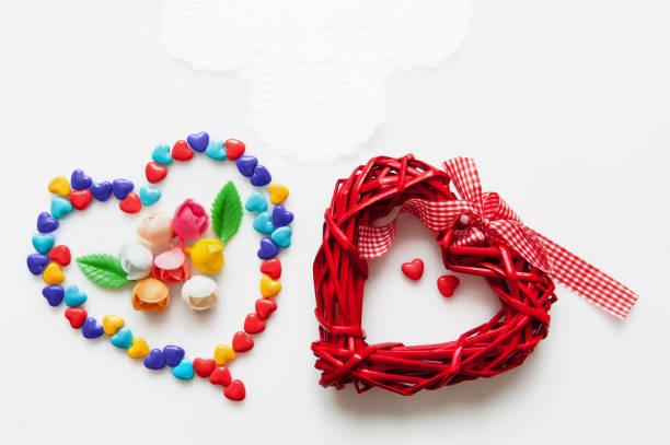 red heart made from a natural material with a fabric bow and heart candies on white background