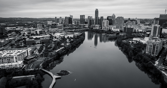 Black and white Austin Texas Aerial Wide View of Entire City with Texas Hill Country background Downtown Skyline and Town Lake on a Calm tranquil monochrome morning with the riverside pedestrian bridge in view along the colorado river