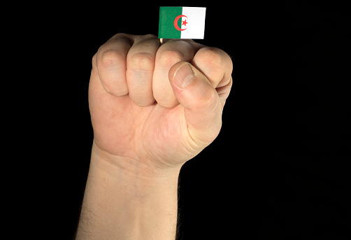 Man hand fist with Algerian flag isolated on black background