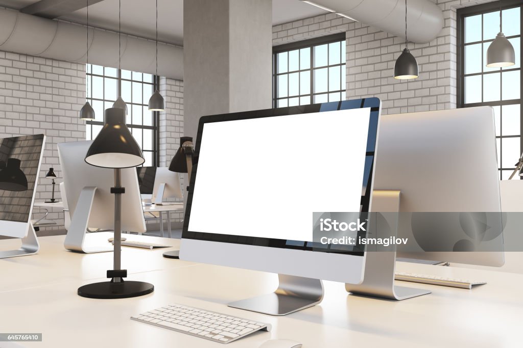 Close up of computer screen, office Close up of a blank computer screen standing in a white office with brick walls. Pipes near the ceiling. 3d rendering. Mock up. Computer Stock Photo