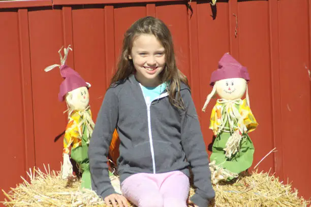 Young girl sitting on a hay bale between Halloween subjects.