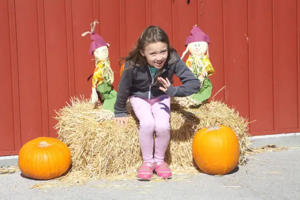 Young girl sitting on a hay bale between Halloween subjects.