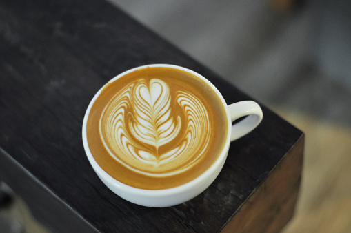 Coffee cup with latte art on the wood bench