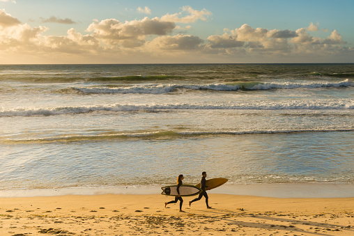 A man and women running into the ocean with their surf boards.