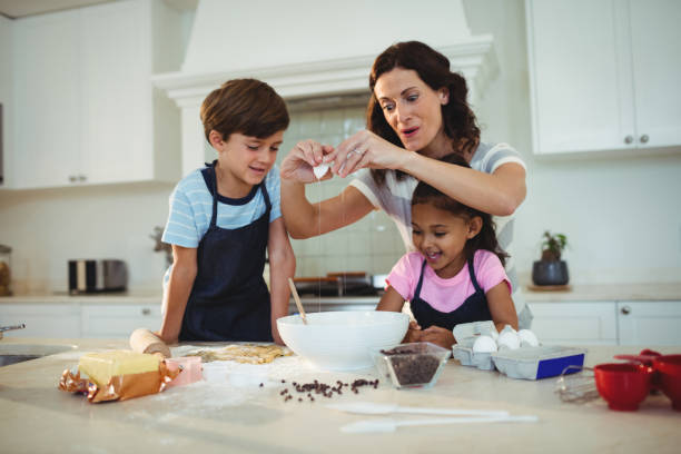 istock Mother and kids breaking egg in the bowl while preparing cookie 645792178