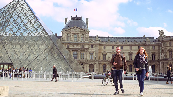 Paris, France - October, 14, 2016: Multiracial tourists walking near glass pyramid in Louvre palace courtyard. Louvre and the Pyramid is one of most known landmarks in Paris.