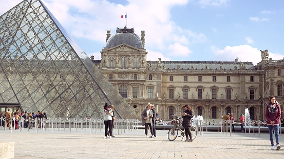 Paris, France - October, 14, 2016: Multiracial tourists walking near glass pyramid in Louvre palace courtyard. Louvre and the Pyramid is one of most known landmarks in Paris.