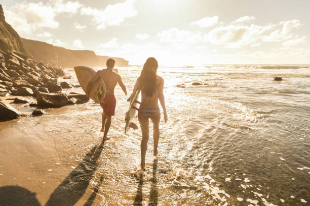 surfisti uomo e donna che corrono in acqua - surfing california surf beach foto e immagini stock