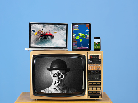 Old fashioned television,modern computer,tablet pc,smartphone on desk.The background is blue wall.There is a black and white image on tv screen while color images on other screens.Shot in studio with medium format camera.
