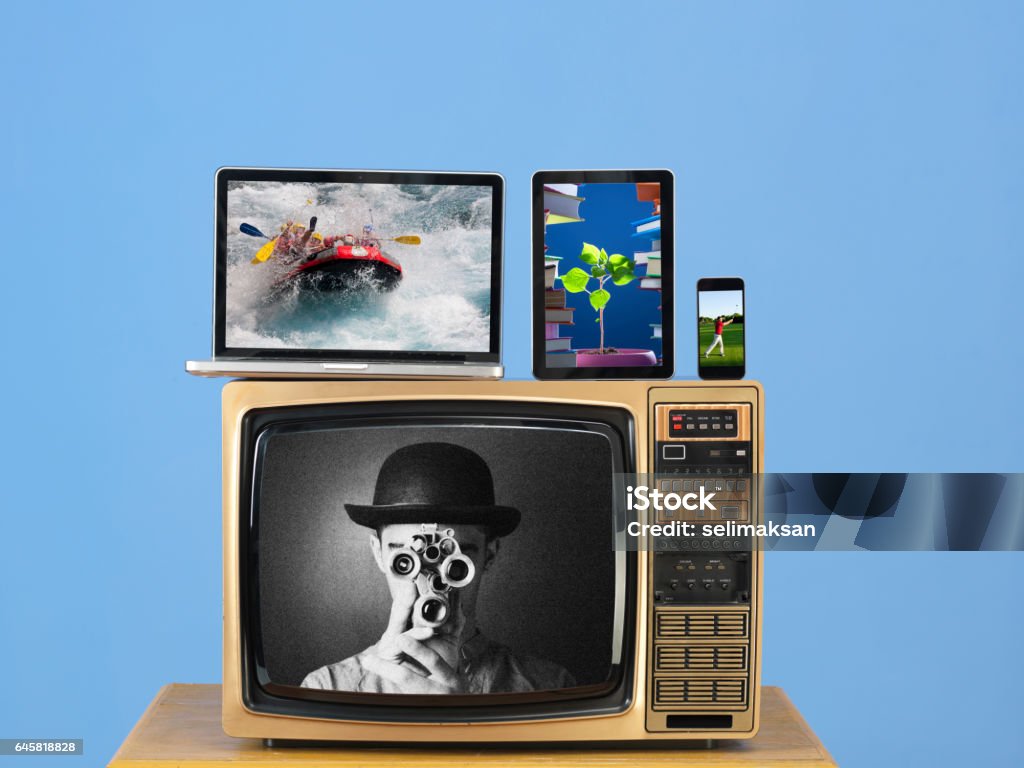 Modern Computer,Smartphone And Tablet Pc On Old Fashioned TV Old fashioned television,modern computer,tablet pc,smartphone on desk.The background is blue wall.There is a black and white image on tv screen while color images on other screens.Shot in studio with medium format camera. Television Set Stock Photo