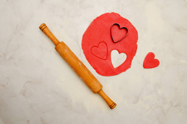 istock Red dough with a a rolling pin and cut out hearts on a white table. Top view, space for text 645825546