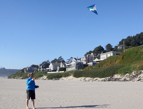 A young man is flying a double stringed kite on the beach of the Oregon coast