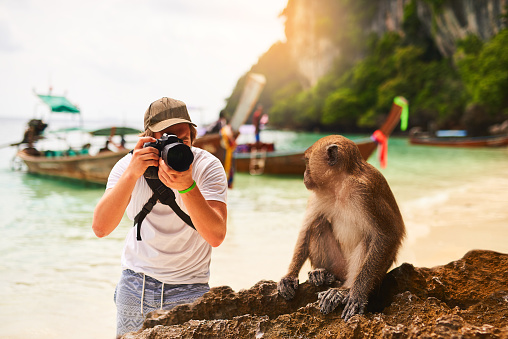 Shot of a young tourist taking a picture of a monkey while exploring a tropical beach