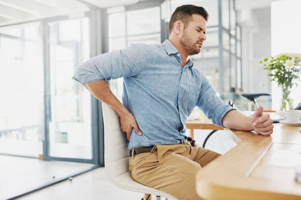 This pain is becoming far too unbearable Cropped shot of a young businessman experiencing back pain while working at his desk uncomfortable stock pictures, royalty-free photos & images