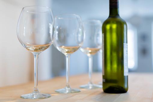 Three clear wine glasses and a bottle of chilled white wine on a wooden table