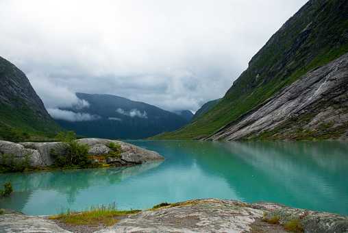 Lake With Mountains In Norway. Cloudy Sky. Peaceful Scenery, Landscape With Rocks And Grass. Greeting Card