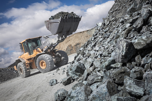 Excavator loads its scoop with unworked mineral from stack
