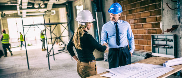 jefe de constructor y arquitecta estrechando la mano en el sitio de construcción - hardhat construction men handshake fotografías e imágenes de stock