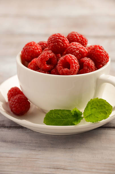 istock Ripe sweet raspberries in white cup on wooden table 645974136